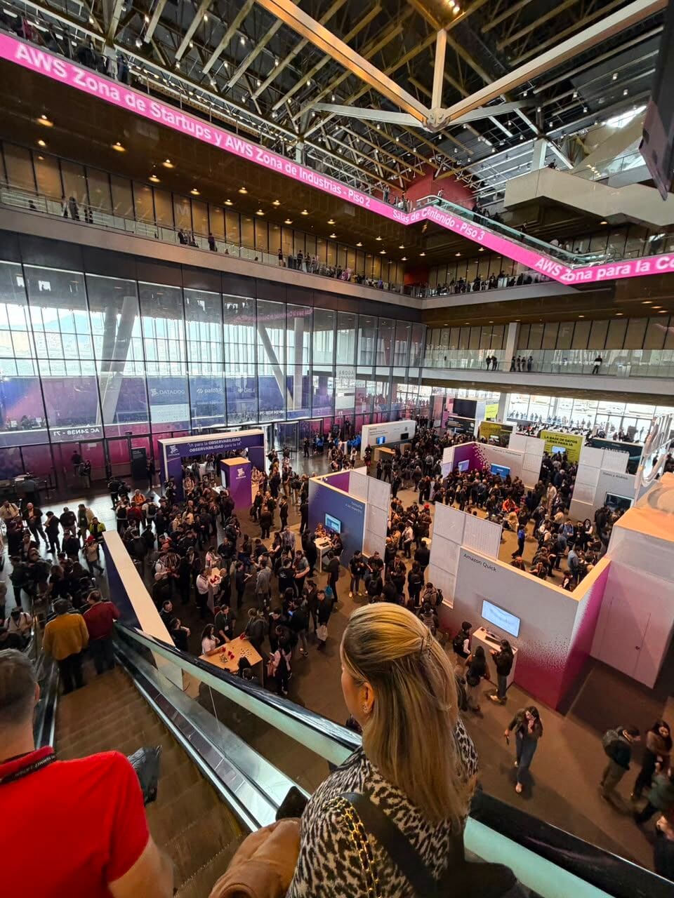 A packed AWS Summit expo floor seen from the escalator, under signs for the startups and industries zones.
