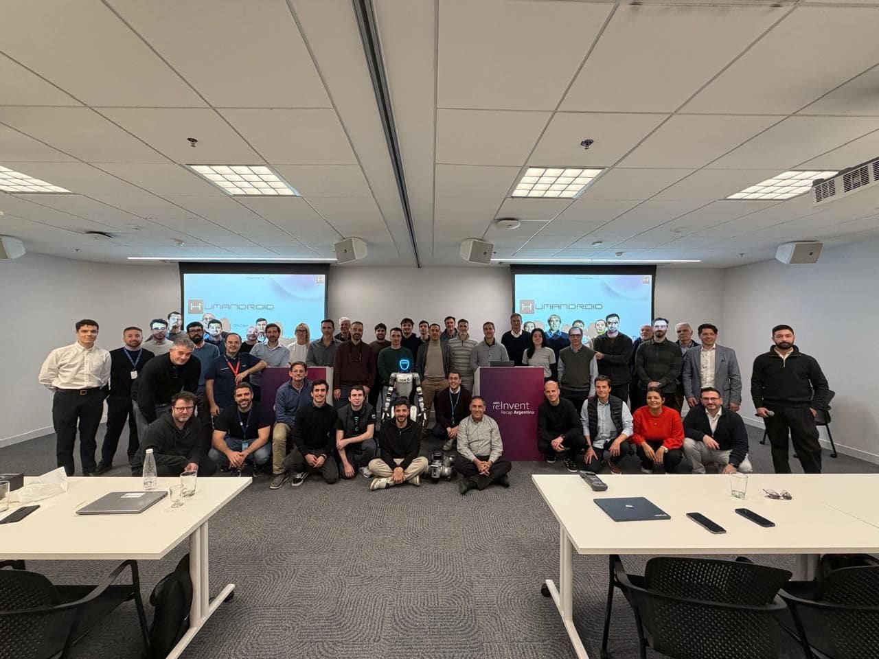 Around forty attendees grouped behind an AWS re:Invent Recap Argentina podium, a humanoid robot standing in front of them.