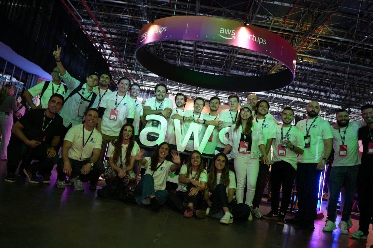 A crew in matching white t-shirts posing under the illuminated aws startups ring on an AWS Summit expo floor.